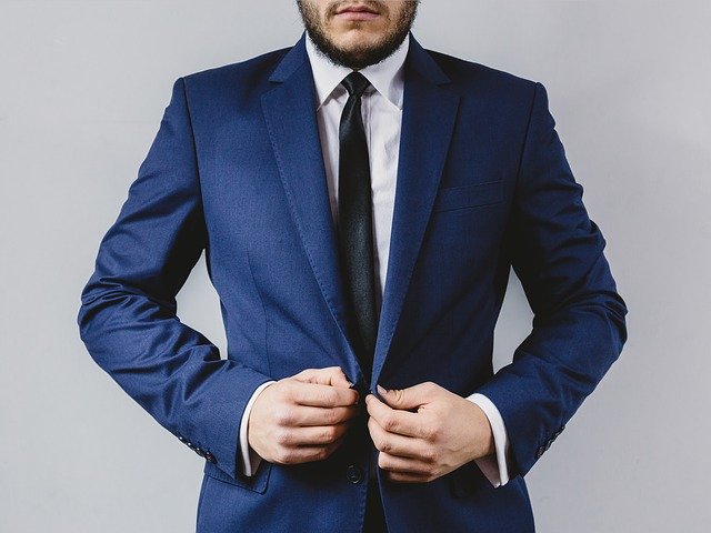 Muž s bradou si zapína modrý oblek.jpg